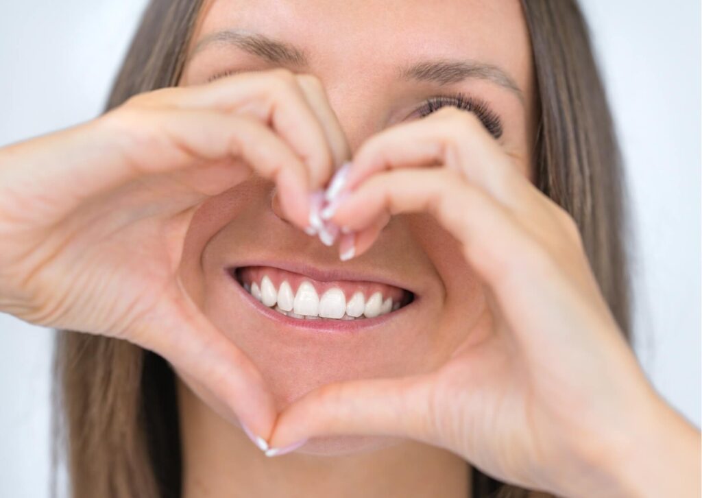 Woman smiling with bright white teeth while making a heart shape with her hands after professional teeth whitening