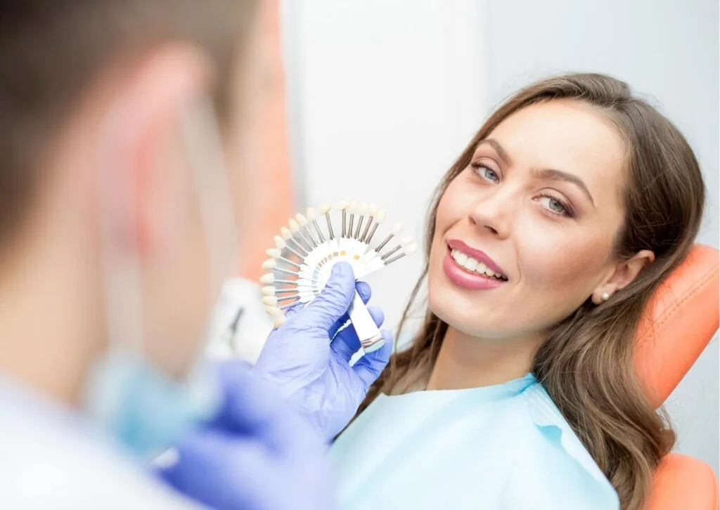 Dentist using a shade guide during a veneer consultation to show what porcelain veneers look like and how they match natural teeth.
