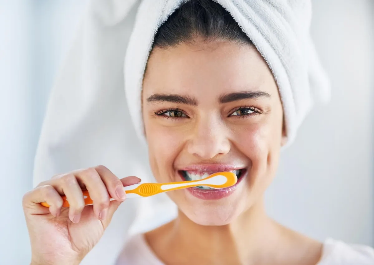 Woman brushing her teeth to maintain oral hygiene and support long-term dental implant longevity.