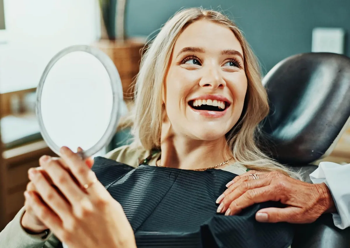 Patient smiling at her new porcelain veneers in a mirror after cosmetic dental treatment.